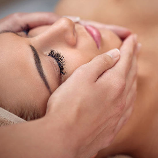 Eine Frau mit geschlossenen Augen genießt eine beruhigende Gesichtsmassage, während ihr Kopf sanft von Händen gehalten wird.