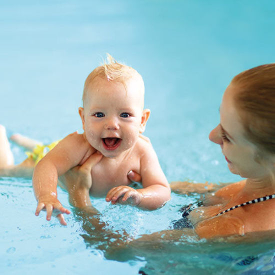 Ein glückliches Baby wird von einer Frau im Schwimmbad gehalten und lacht fröhlich im Wasser.