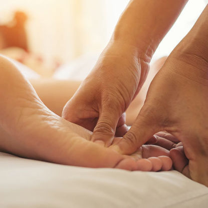 Nahaufnahme einer wohltuenden Fußmassage in entspannter Atmosphäre mit warmem Licht.