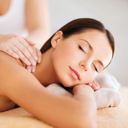 Eine Frau liegt entspannt mit geschlossenen Augen auf einer Massageliege, während eine Therapeutin ihr den Rücken massiert.