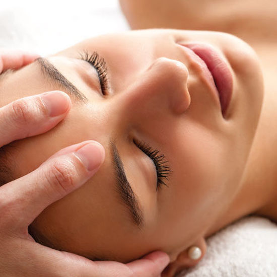 Eine Frau mit geschlossenen Augen erhält eine entspannende Stirnmassage in ruhiger Atmosphäre.