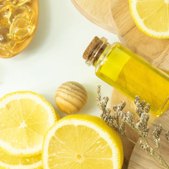 Arrangement aus Naturkosmetik-Zutaten: eine aufgeschnittene Zitrone, Massagekugeln aus Holz, ein Glas mit gelbem Öl, getrocknete Lavendelzweige und weitere Naturprodukte auf runden Holzunterlagen.