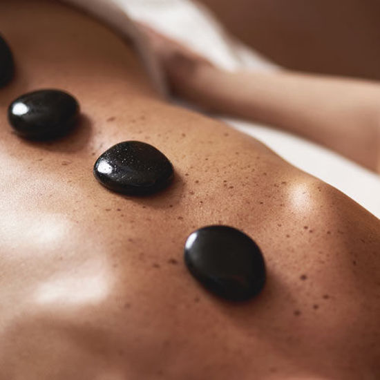 Glatte schwarze Massagesteine liegen auf dem Rücken einer Person während einer Hot-Stone-Behandlung.