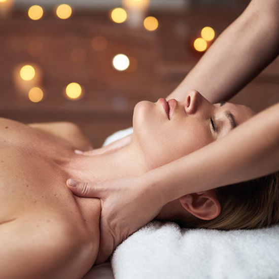 Eine Frau erhält eine entspannende Nackenmassage in ruhiger Atmosphäre mit warmem Kerzenlicht im Hintergrund.