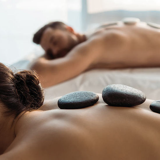 Ein Paar liegt entspannt nebeneinander bei einer Hot-Stone-Massage in ruhiger Atmosphäre.