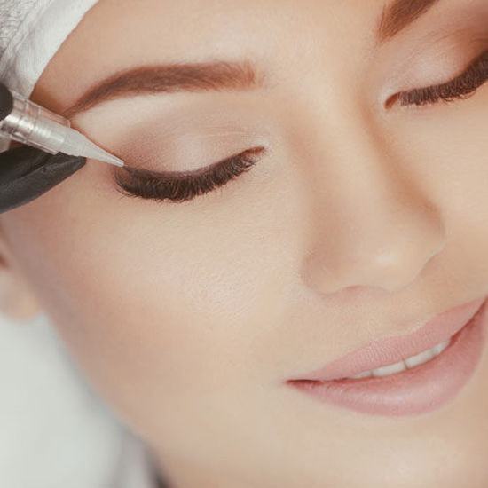 Frau mit geschlossenen Augen erhält ein dauerhaftes Augen-Make-up mit einem feinen Pigmentiergerät am oberen Lidrand.