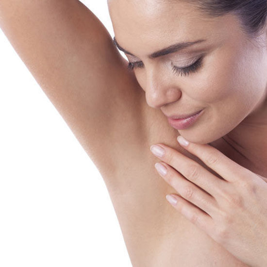 Eine Frau betrachtet lächelnd ihre glatte Achsel, mit geschlossenen Augen und sanfter Hand auf der Schulter, vor weißem Hintergrund.