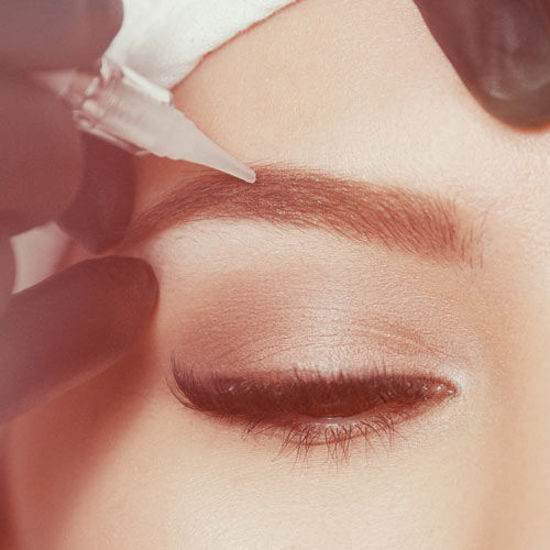 Aufnahme einer lächelnden Frau. Ihre Augenbrauen bekommen eine Behandlung mit Permanentem Make Up.