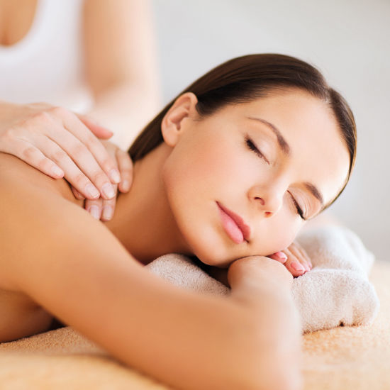 Eine Frau liegt entspannt mit geschlossenen Augen auf einer Massageliege, während eine Therapeutin ihr den Rücken massiert.