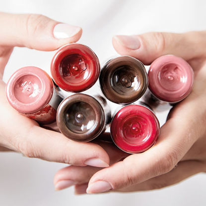 Nahaufnahme von Händen, die mehrere geöffnete Farbtuben in verschiedenen Rot- und Brauntönen halten.