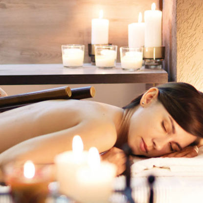 Eine Frau mit dunkelbraunen Haaren liegt entspannt bei einer Wellnessbehandlung mit Bambusstäben, umgeben von warmem Kerzenlicht.