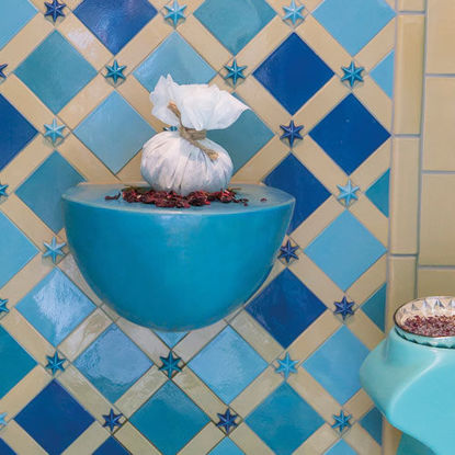 Blick auf einen stilvoll gestalteten orientalischen Ruhebereich mit türkisfarbenen Liegeflächen und einer kunstvoll gefliesten Wand in Blau- und Beigetönen. In der Mitte befindet sich ein dekorativer Wasserbrunnen.